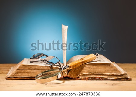 book magnifying glass  and glasses on wooden table and blue background