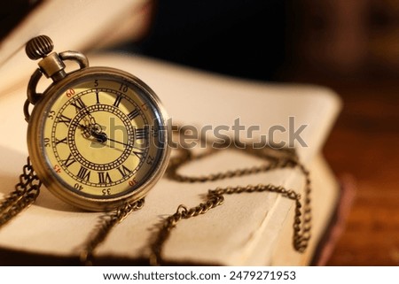 Pocket clock with chain and book on table, closeup. Space for text