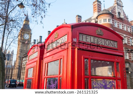 Famous red telephone box with Big Ben on background in a sunny early morningin London. There are also some chimneys and trees.