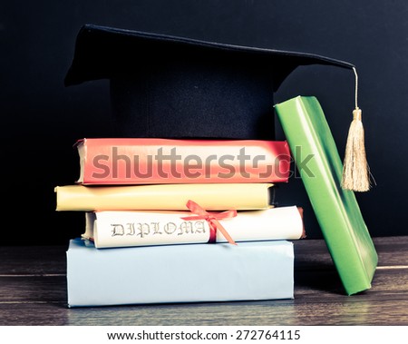 A mortarboard and graduation scroll, tied with red ribbon, on a stack of books 