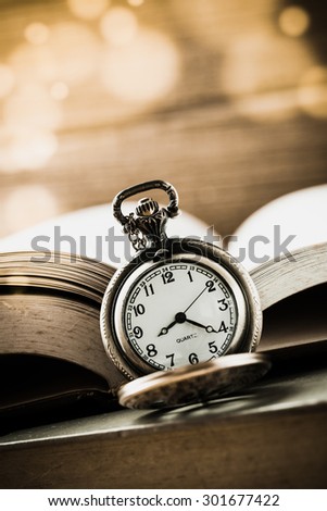 Retro clock and old book with bokeh on wooden background