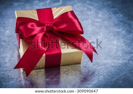 Wrapped golden box with red ribbon bow close up view.