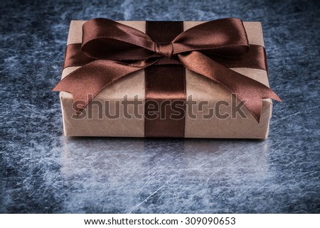 Giftbox with brown ribbon on scratched metallic background holidays concept.