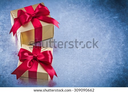 Packed golden gifts with red bows on scratched metallic background.