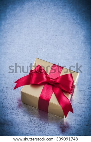 Boxed golden present with red ribbon on metallic background.