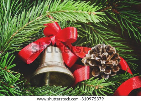Christmas bell with a red ribbon, pine-needles and cones on old wooden background, selective focus