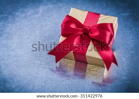 Packed golden box with red bow on scratched metallic background.