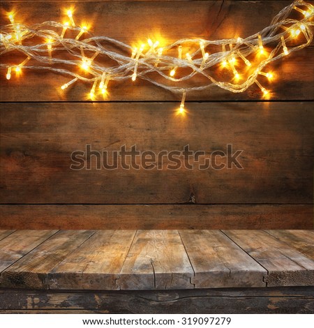 wood board table in front of Christmas warm gold garland lights on wooden rustic background. filtered image. selective focus
