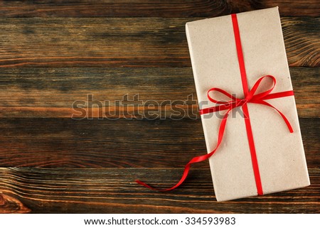 Gift box with red ribbon on wood background