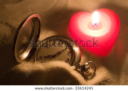 Antique watch covered with sand and a red heart-shaped candle