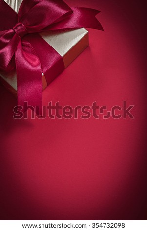 Wrapped giftbox with tied bow on red background holidays concept.