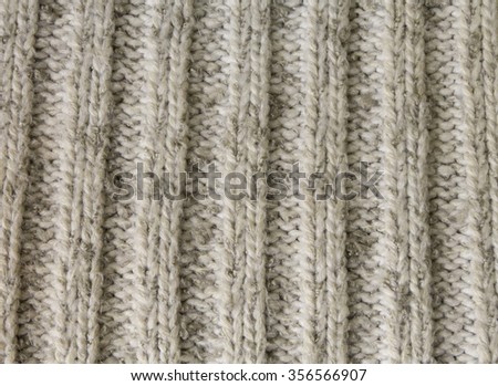 Closeup shot of a texture of white and grey wool hand knit fabric with vertical relief design.
