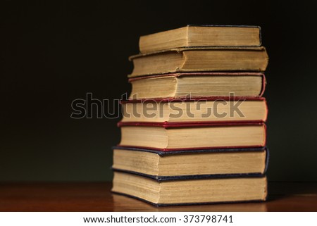 Stack of vintage, shabby, well used books on a wood desk in front of a dark wall with plenty of copy space.