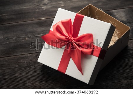white gift box with red ribbon bow on dark wood background
