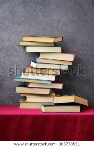 The stack of books in the colored cover on the table with a red tablecloth on the background of the old wall. The vertical frame.