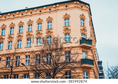Low Angle Architectural Exterior of Low Rise Residential Building with Yellow Facade and Classical Sculptural Details and Small Corner Balconies on Overcast Day with Bare Trees