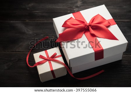 white gift box with red ribbon bow on dark wood background