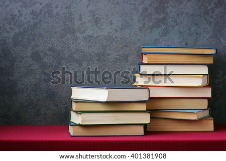 Books with colored covers on the table with a red tablecloth on the old grey wall background with texture.