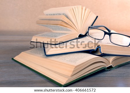Pile of books and eyeglasses on it on wooden table, close up