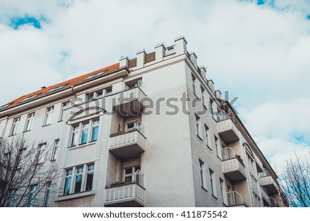 Low Angle Architectural Exterior of Corner of Modern Low Rise Residential Apartment Building with Small Balconies and White Facade, Framed by Cloudy Sky and Bare Trees in Berlin, Germany