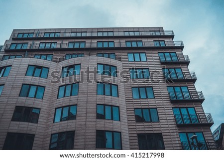Low Angle Architectural Exterior of Modern Low Rise Residential Apartment or Condominium Building with Brown Stone Facade and Small Corner Balconies in Urban City Setting with Overcast Sky