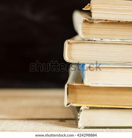 A stack of books on a desk with blackboard in the background