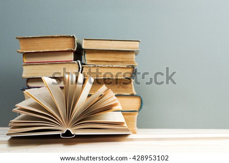 Open book, stack of hardback books on wooden table. Back to school. Copy space.