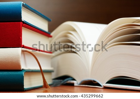 Close up of books and large book pages.
Stack of books and open book on wooden table.
