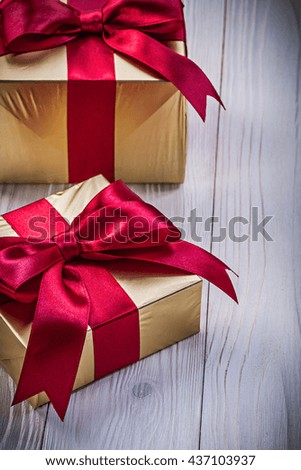 Present boxes in golden paper with red knots on wooden board holidays concept.