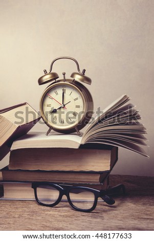 A pile of books and eyeglasses and alarm clock ,with a retro effect.
