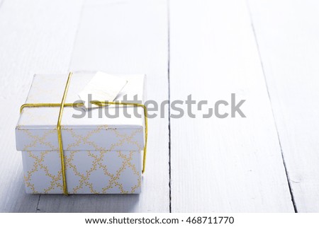white gift box with golden string and card on bright wood table