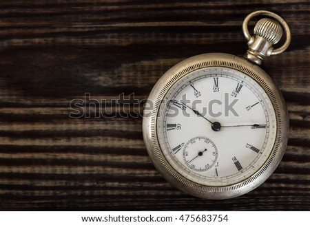 Old pocket watch on grungy wooden desk.
