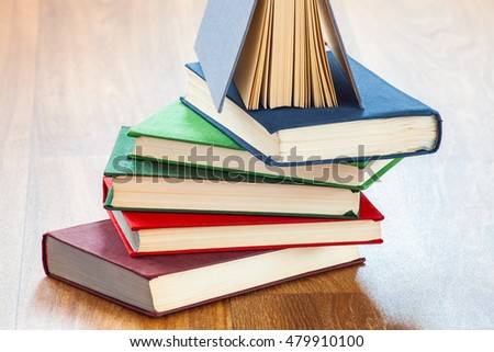 Books in a firm cover lie one on one on a surface of a wooden table.