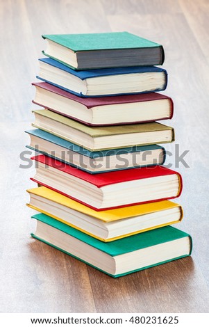 Books in a firm cover lie one on one on a surface of a wooden table.