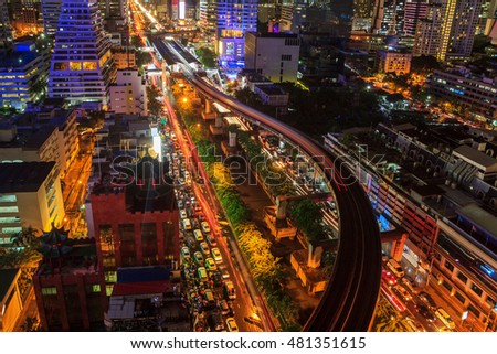 Colorful night in Bangkok Traffic density Skytrain and the growth of the modern city.Panoramic and perspective view light blue background of glass high rise building skyscraper commercial of future.