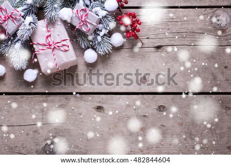 Wrapped christmas presents, fur tree branches, red berries on aged wooden background. Drawn snow effect. Selective focus. Top view. Place for text.