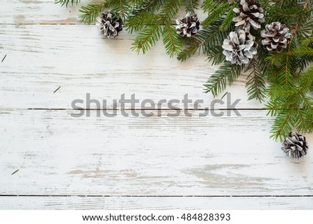 Christmas tree branch with pinecones on white wooden table.