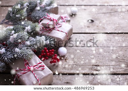 Wrapped christmas presents, fur tree branches, red berries on aged wooden background. Selective focus is on berries. Drawn snow effect. Place for text.
