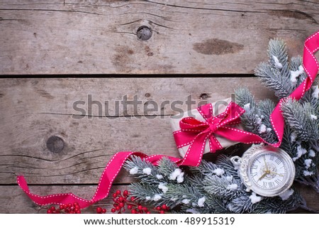 Wrapped christmas gift box, decorative clock and fur tree branches on aged wooden background. Selective focus. Place for text.