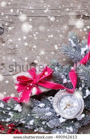 Wrapped christmas gift box, decorative clock and fur tree branches on aged wooden background. Selective focus. Place for text. Drawn snow.
