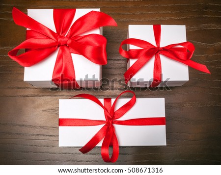 three white gift boxes with red ribbon on wooden background