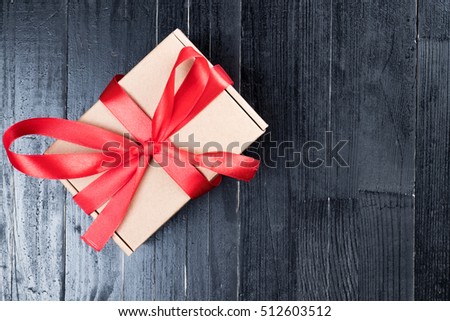 Natural paper box with red ribbon bow on black natural wooden table. Christmas or Valentine's Day abstract concept. Copy space to the right.