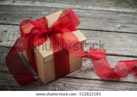 Craft paper gift box with red bow on old wooden table. Place for text