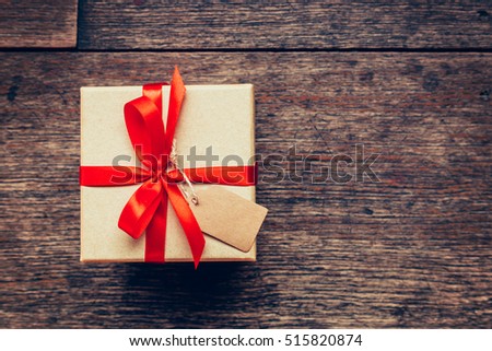 View above brown gift box and red ribbon with tag on wood background with space.