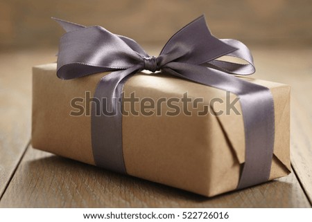 rustic craft paper gift box with lilac ribbon bow on wood table, shallow focus