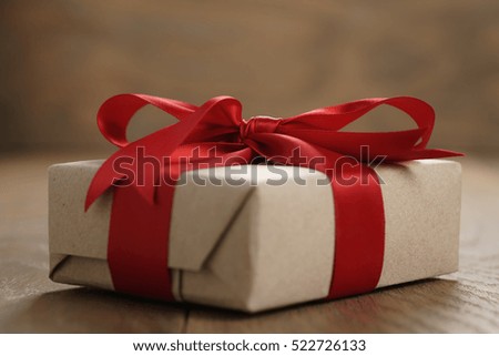 rustic craft paper gift box with red ribbon bow on wood table, shallow focus