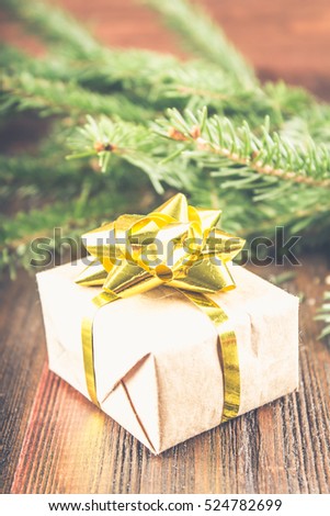 gift with golden bow under the Christmas tree branches on a wooden background.