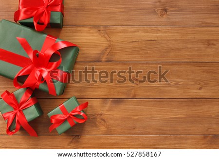 Presents for any holiday concept. Gift boxes frame, top view with copy space on wood table background. Border of green packages with red satin ribbons for christmas, valentine day or birthday