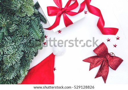 Flat lay, Top view Christmas composition on white background. Natural green pine wreath, gift box with fabric tape, red bow, Santa cap, spiral ribbon, stars confetti. Xmas decor.
