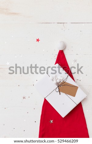 Top view on nice Christmas gift wrapped in white gift paper, Christmas tree decorations in Santa's hat on wooden background with sparkling stars. New Year, holidays and celebration concept.